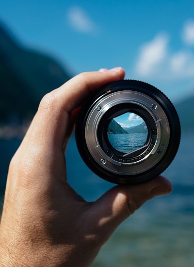 Een hand houdt een lens vast waardoor je een scherp en verkleind beeld ziet van bergen en water